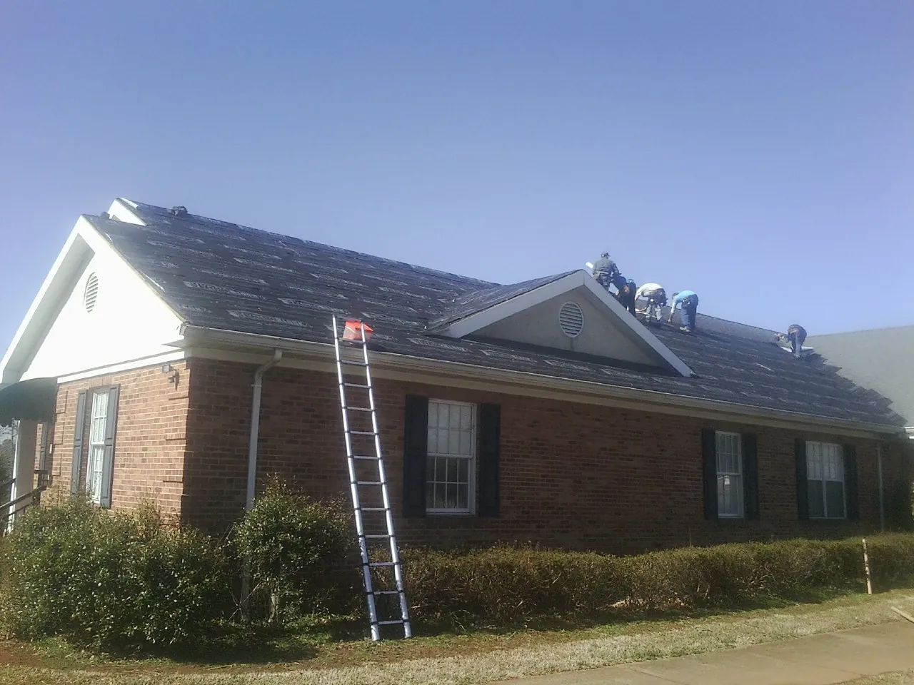 Crew tearing shingles off a brick ranch roof with a ladder set — Emergency Roof Repair work by our crew in Cheswold