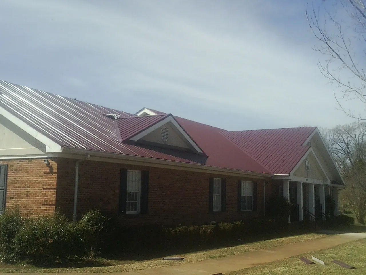 Red metal roof with gabled entries on a long brick building, from a Hail Damage Roof Repair job in Cheswold