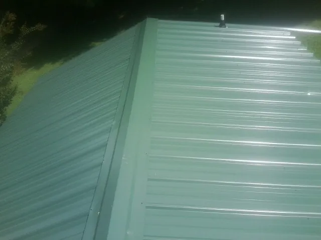 New green metal panels meeting at the ridge of a roof — Flat Roof Repair work by our crew in Cheswold