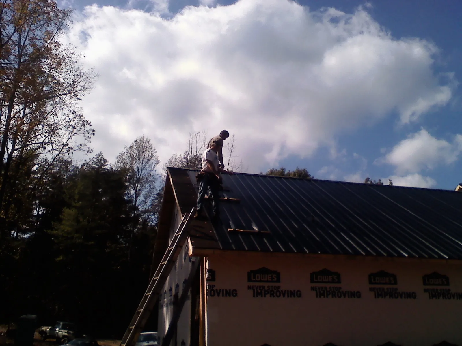 Roofer fastening dark metal panels high against a cloudy sky, from a Roof Inspection job in Cheswold