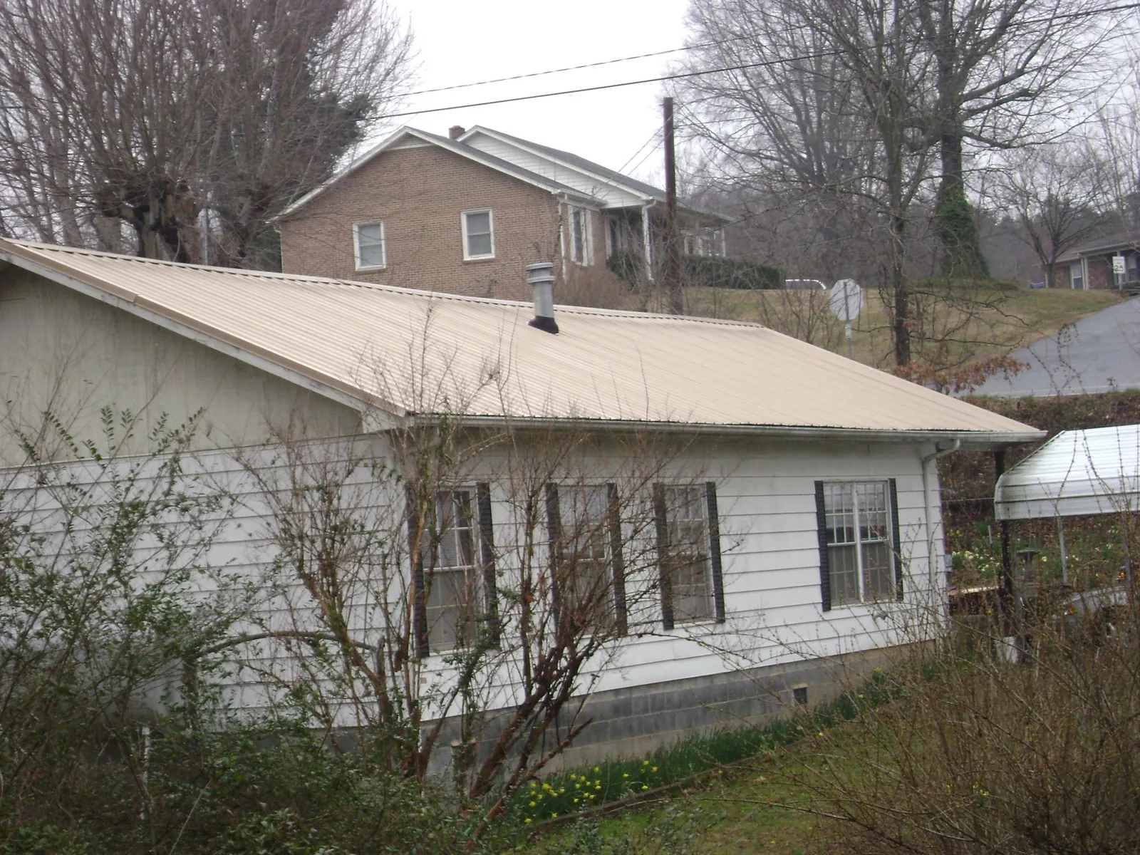 Tan metal roof on a white sided house set into a hillside — Commercial Roofing by Roofing Brothers in Cheswold